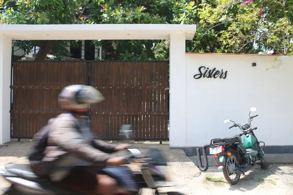 The guesthouse gate on Welhengoda Road — dark timber, a white wall carrying the old script wordmark.