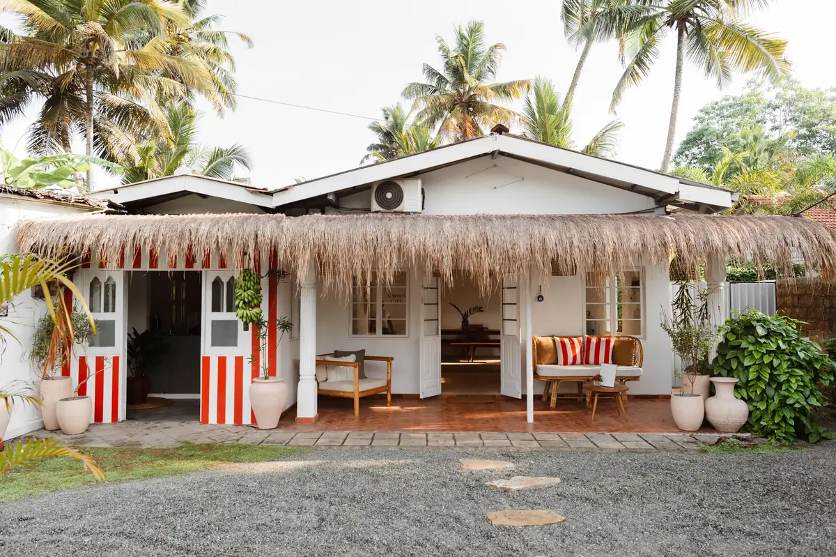 Sisters Kabalana from the lane — red and white striped doors folded open under a thatched eave, palms behind.
