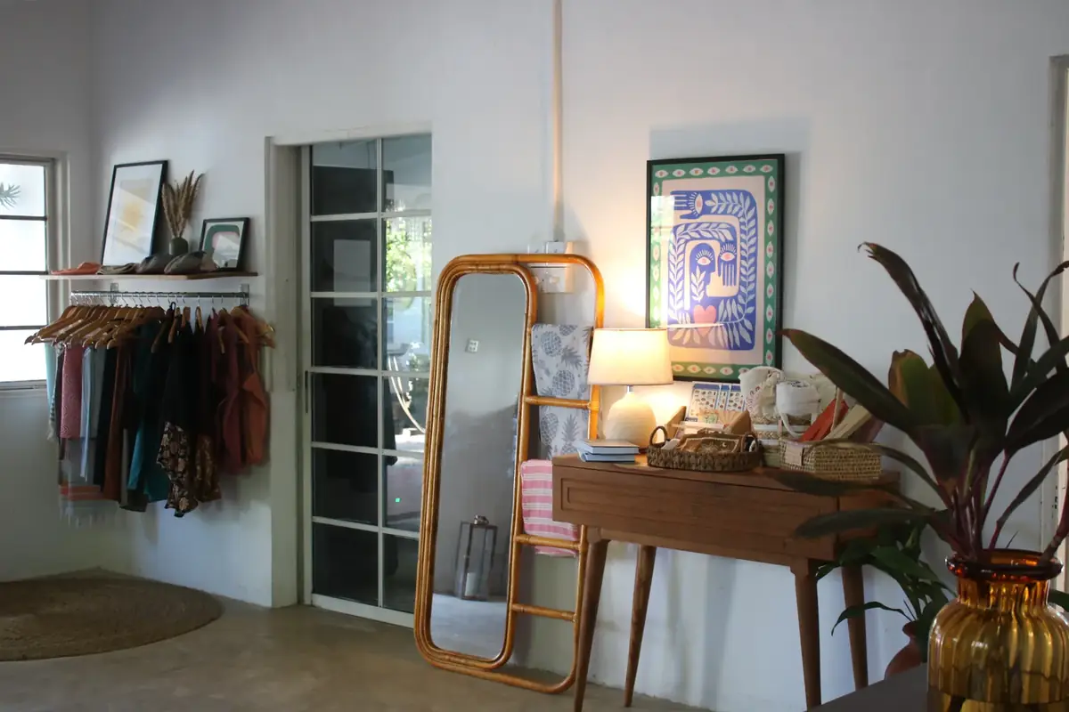 The showroom — a clothing rail, a rattan floor mirror, a console of small goods, prints and a lamp.