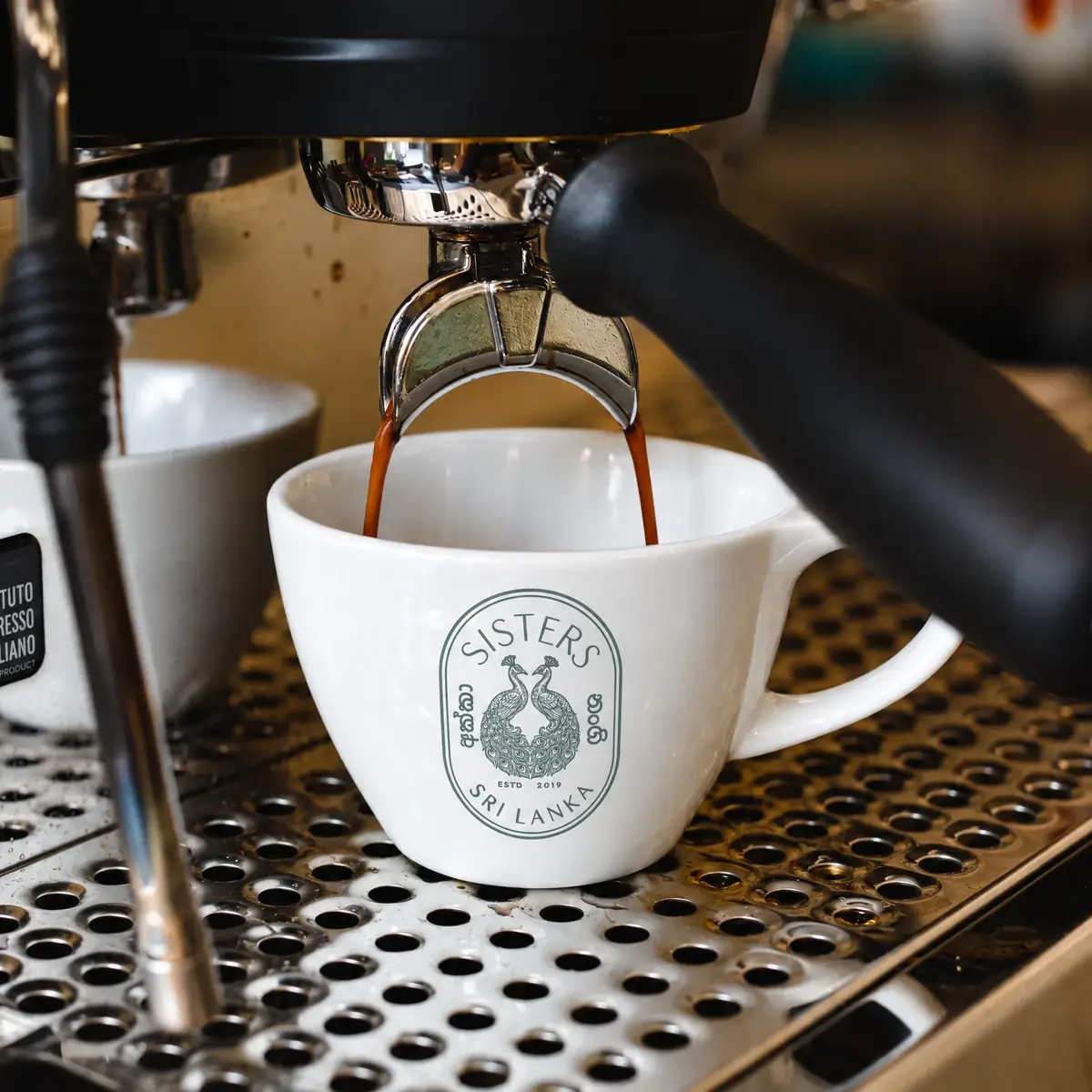Espresso pulling into a Sisters cup on the machine tray, the peacock crest facing out.