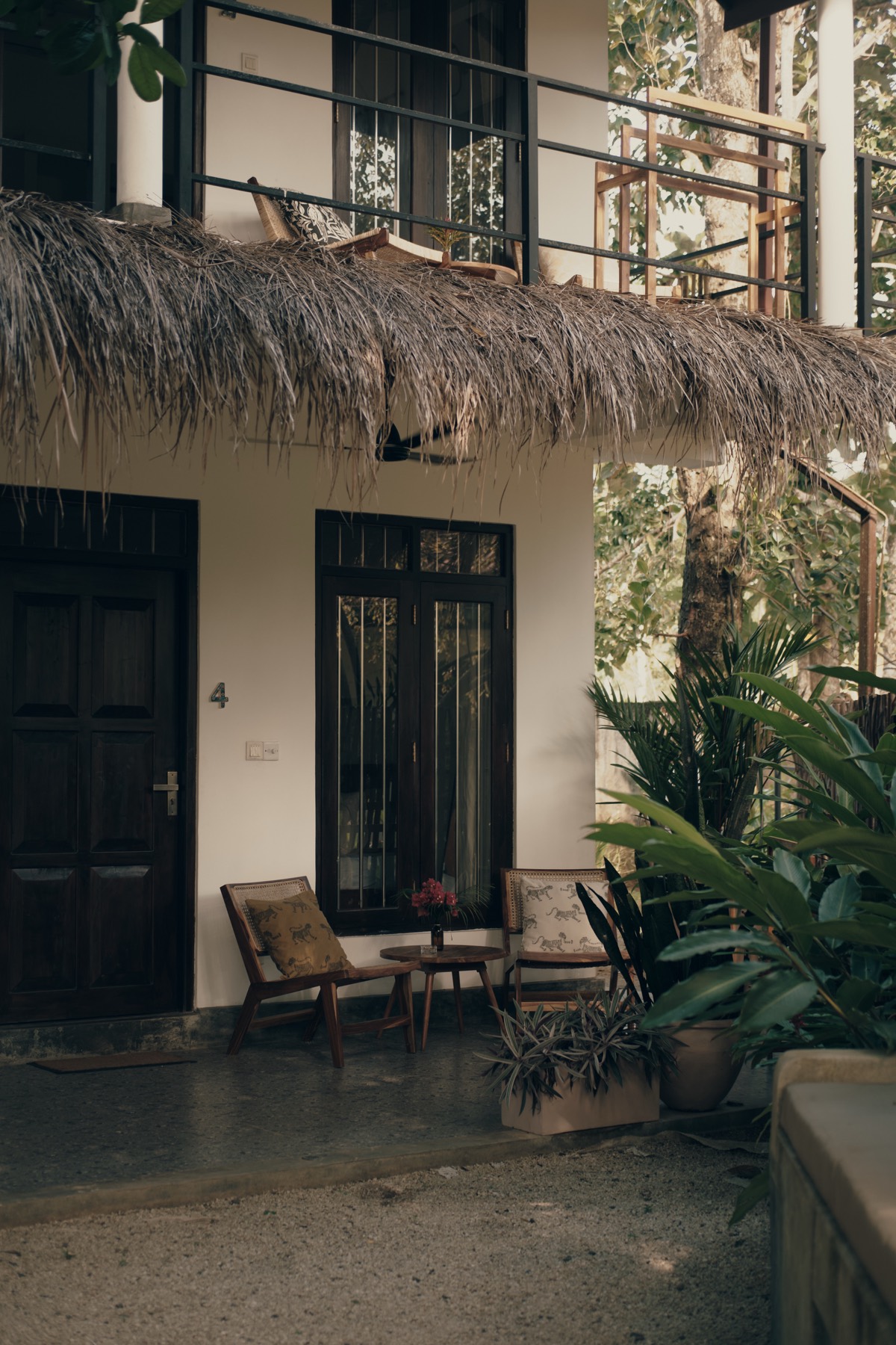 A guesthouse room at Sisters Away — dark timber door, thatched eave, potted plants and planter chairs on the veranda.